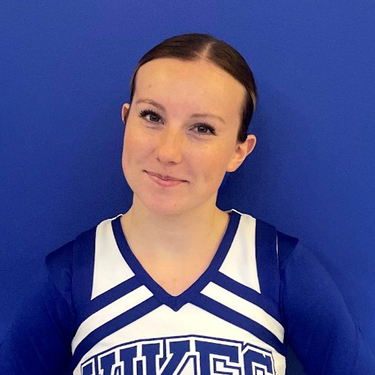 Aliyah is wearing a blue and white athletic uniform. She is standing in front of a blue background and smiling at the camera.