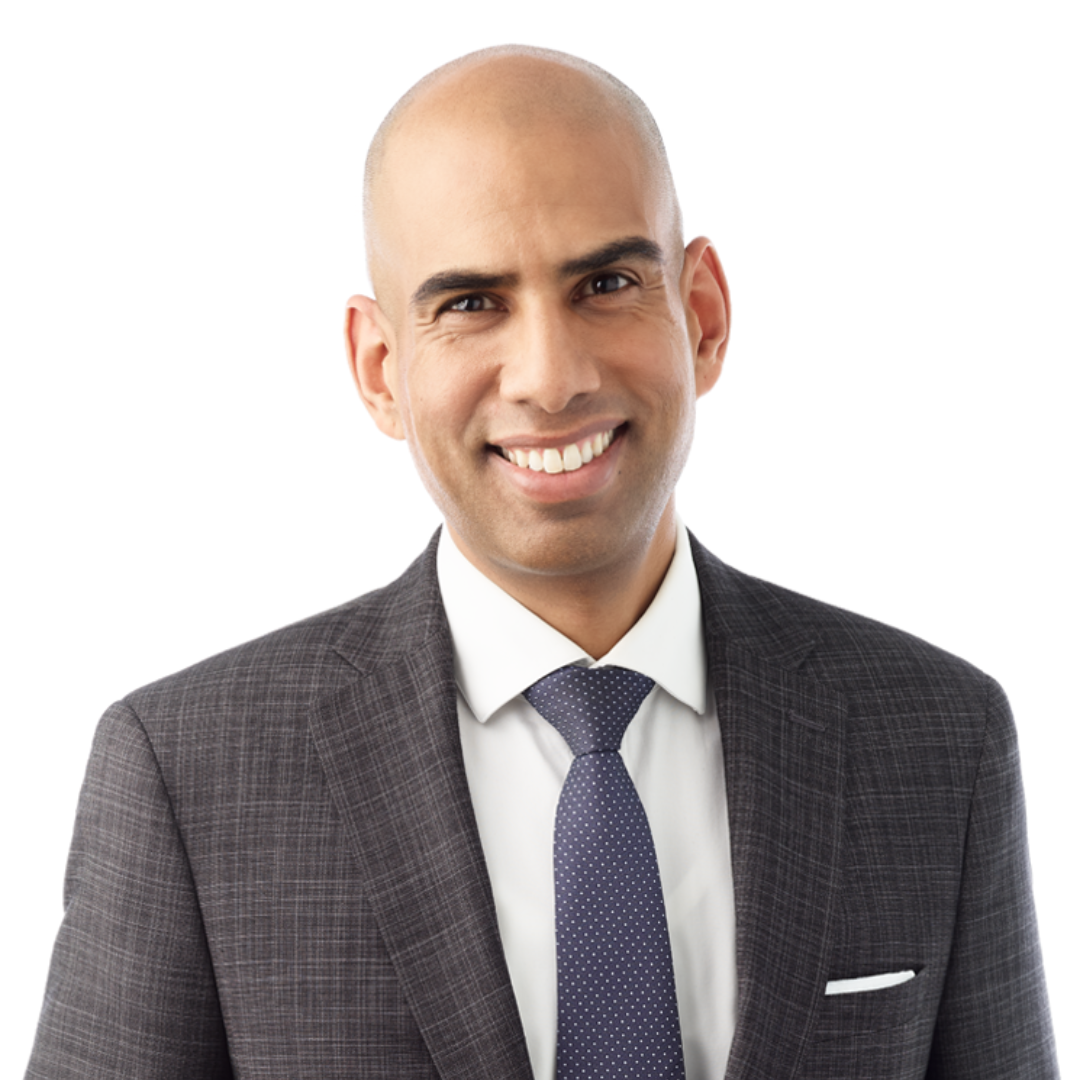 Brendon Pooran is smiling for a close-up headshot. He is wearing a grey striped blazer with a white dress shirt and blue polka dot tie.