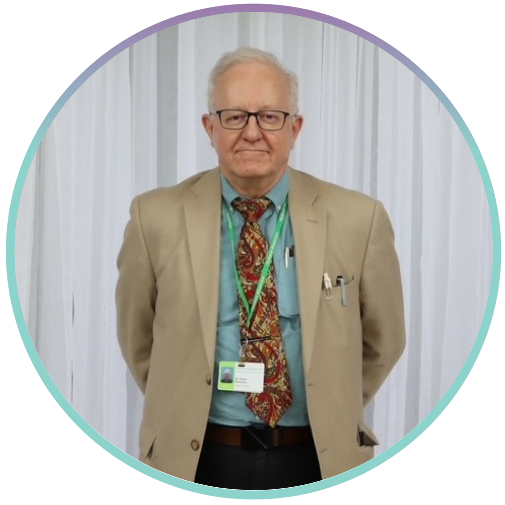 Dr. Peter Rumney is posing for a photo wearing a beige suit with a blue tie. He is smiling with his hands behind his back in front of a white curtain.
