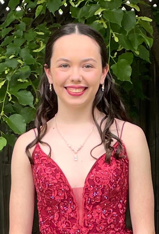 Alaina is wearing a formal red dress. She is standing in front of a tree and smiling at the camera. 