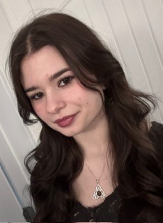 Catherine Derouard is posing for a selfie in her home. She has long, dark hair and is wearing a black shirt.