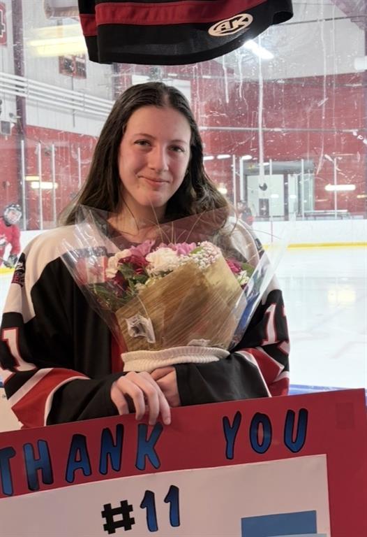 Chelsea Kulawic is posing for a photo in her hockey gear while holding a sign that says, Thank You.