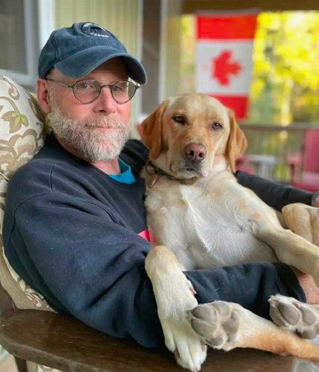 David Schaller is posing for a photo with his golden lab on his lap.