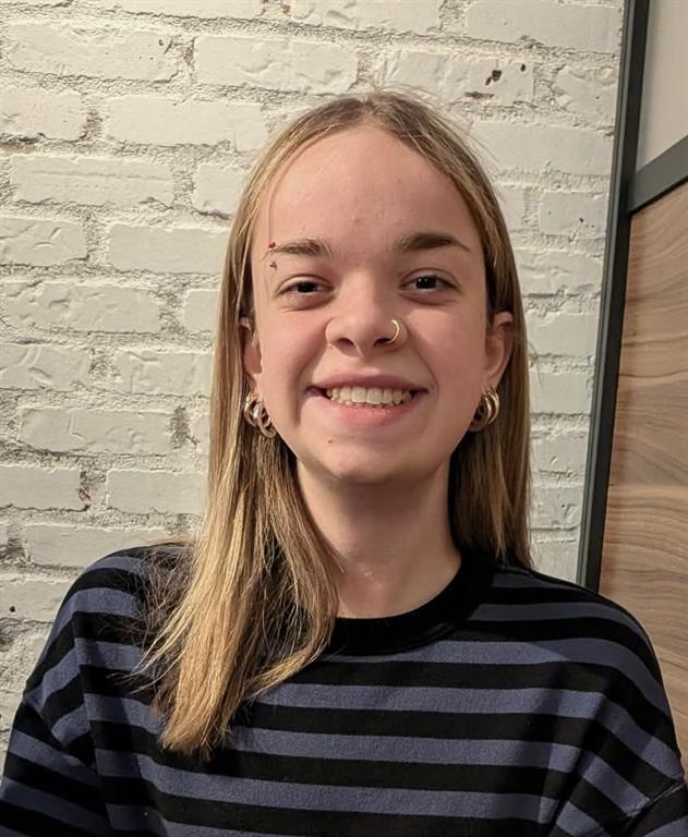 Jocelyne Hewitson is smiling for a photo in front of a painted white brick wall.