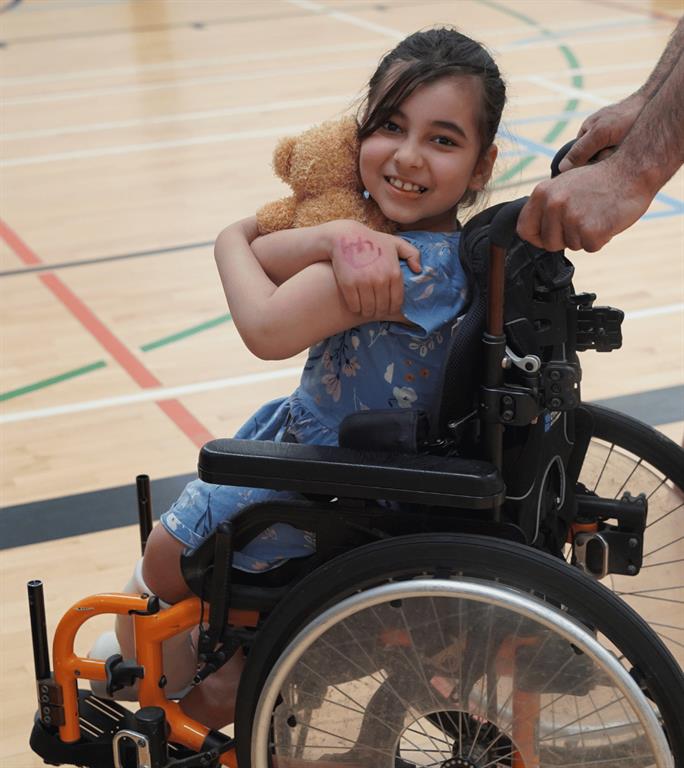 A young girl is smiling for a photo while sitting in her wheelchair.